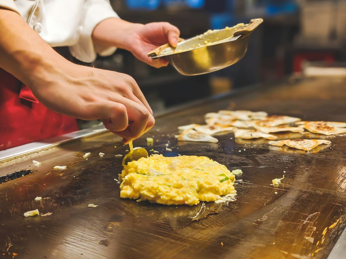 A chef making okonomiyaki on a grill.